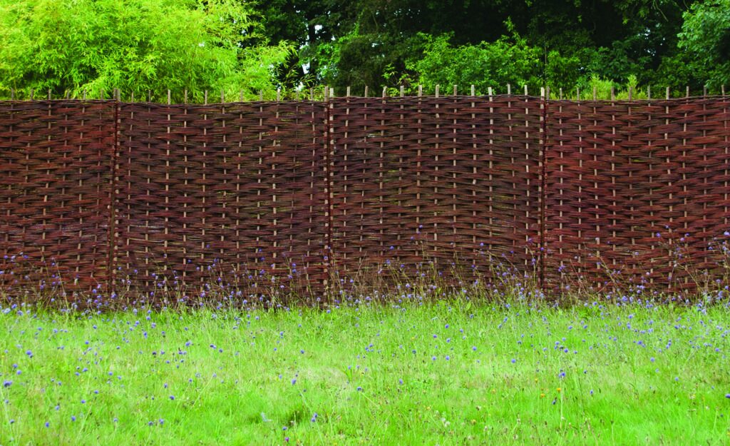 Run of red-brown handwoven willow hurdle fence panels behind a meadow of cornflowers